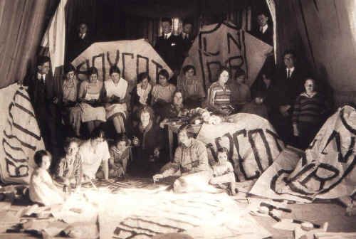 Grupo de mujeres y niñas sentadas en una habitación rodeadas de mantas con la palabra boicot.
